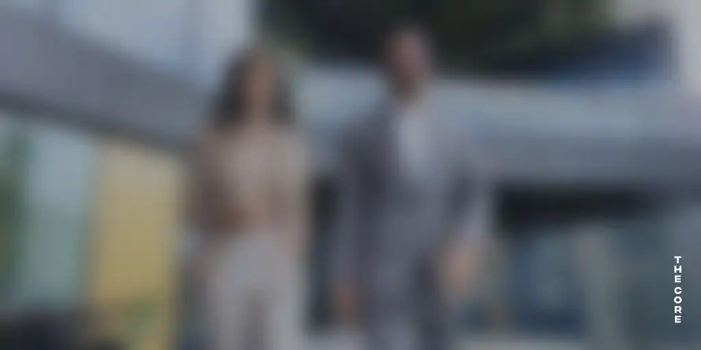 Pareja caminando en un entorno arquitectónico contemporáneo, mostrada de forma intencionadamente desenfocada, con la marca The Core como elemento visual, simbolizando foco, acompañamiento y liderazgo compartido.